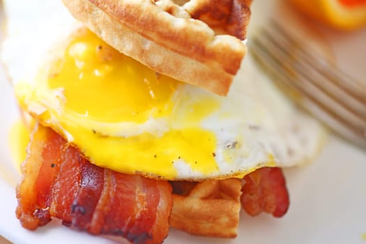 Sandwich of waffle, bacon and fried egg with yolk broken
