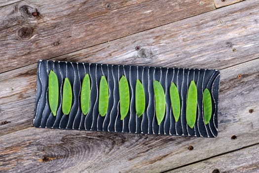 elongated bowl with green peapods  on wooden ground