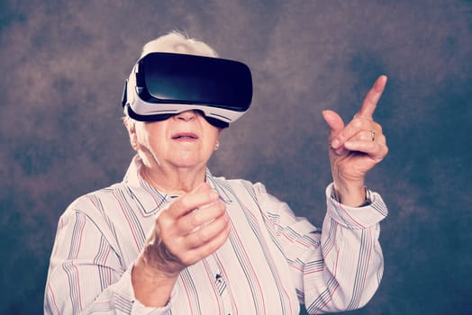 gray hairy elderly woman using virtual reality glasses and looking surprised