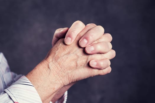 wrinkly hands of  elderly woman praying in front of dark background
