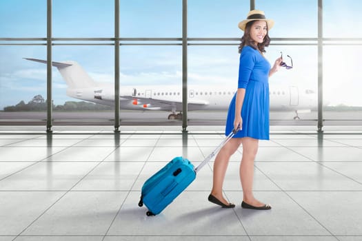 Smiling asian traveler woman with suitcase walking on terminal airport