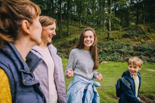Teenage girl and her little borther are talking to their mother and grandmother as they hike through the woodlands together.