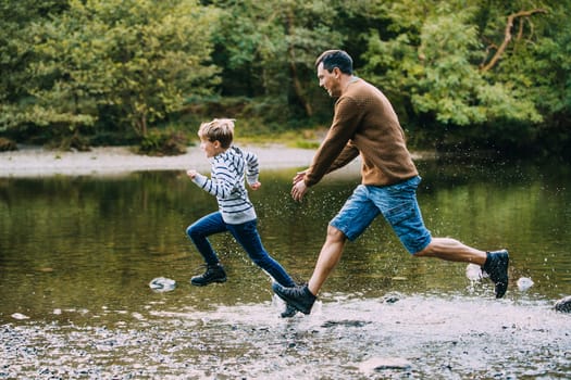 Little boy is being chased in to the lake by his father while they are out hiking.