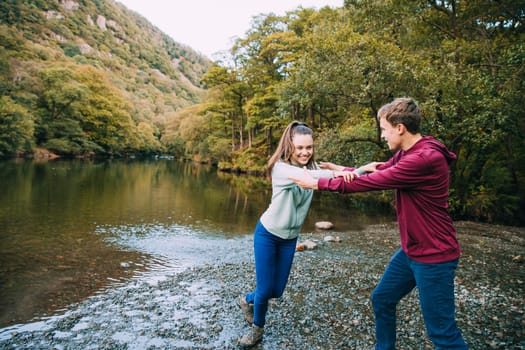 Teenage boy is being pushed away by his sister as he is trying to push her in to a lake they have found while hiking.