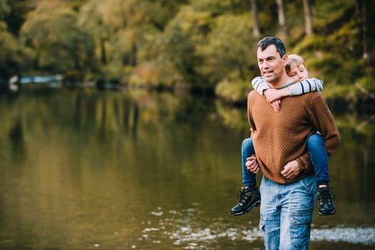 Little boy is receiving a piggyback from his father while they are hiking through the Lake District.