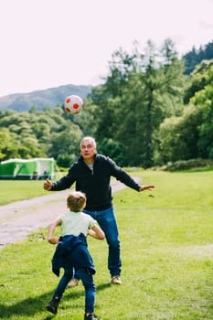 Little boy is playing football with his grandad in the campsite they are staying in.
