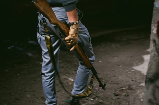 Athletic man in gray clothes with a carbine gun in his hand. Close-up of tactical gloves with weapons