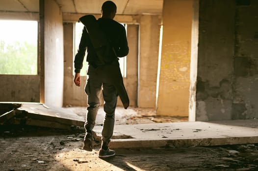Athletic man walks through the ruins, with a cover for a gun for weeping, warm rays of light in the window