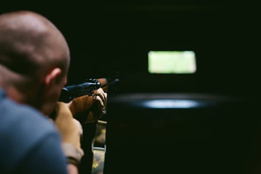 Athletic man in gray clothes with a carbine gun in his hand. Close-up of tactical gloves with weapons. Aiming at distance, rear view