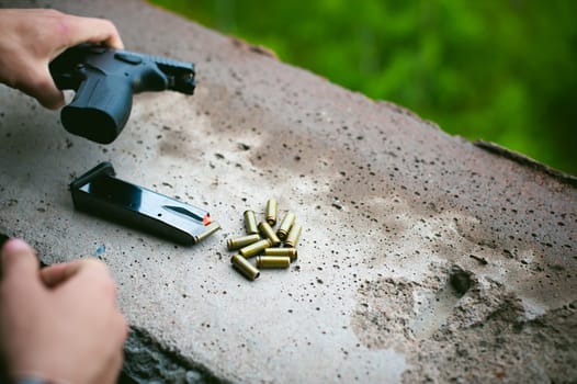 Man charges clip of pistol with bullets. Photo hands of paramilitary, reloading weapons. Preparation for shooting