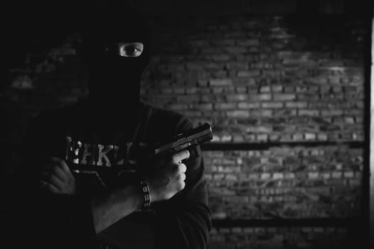 Athletic man in a balaclava, ski mask on his head, holds a gun in his hand, with his arms crossed over his chest