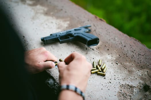 Man charges clip of pistol with bullets. Photo hands of paramilitary, reloading weapons. Preparation for shooting