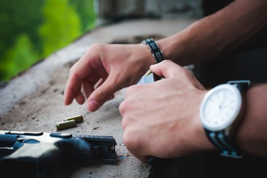 Man charges clip of pistol with bullets. Photo hands of paramilitary, reloading weapons. Preparation for shooting