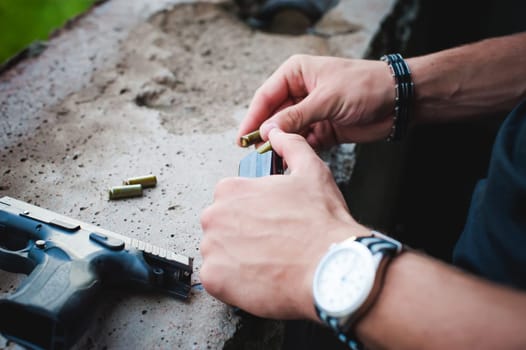 Man charges clip of pistol with bullets. Photo hands of paramilitary, reloading weapons. Preparation for shooting