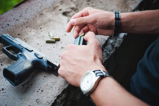 Man charges clip of pistol with bullets. Photo hands of paramilitary, reloading weapons. Preparation for shooting