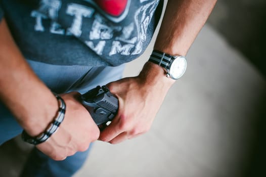 Dangerous athletic man, holds a gun in his hands, close-up. Wristband and watch