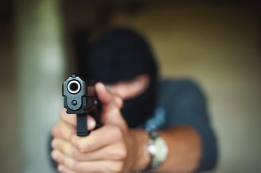Athletic man in a balaclava, holds a pistol in his hand, is threatened with shooting, aiming