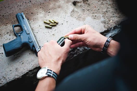 Man charges clip of pistol with bullets. Photo hands of paramilitary, reloading weapons. Preparation for shooting