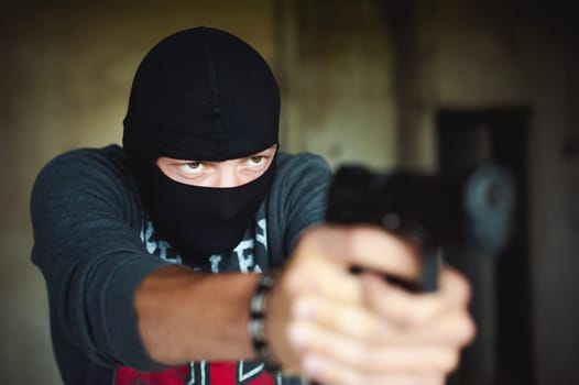 Athletic man in a balaclava, holds a pistol in his hand, is threatened with shooting, aiming