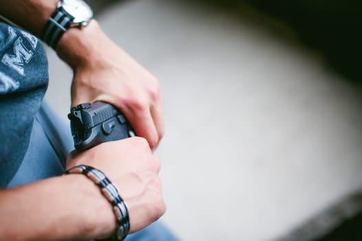 Dangerous athletic man, holds a gun in his hands, close-up. Wristband and watch