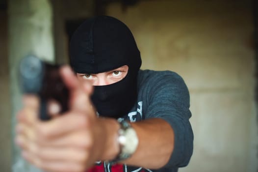 Athletic man in a balaclava, holds a pistol in his hand, is threatened with shooting, aiming