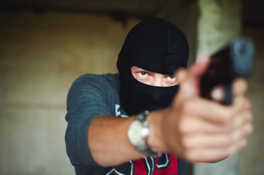 Athletic man in a balaclava, holds a pistol in his hand, is threatened with shooting, aiming