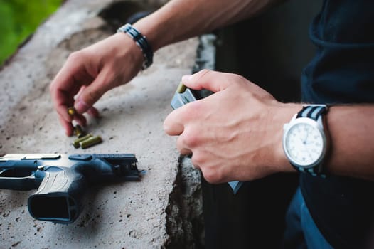 Man charges clip of pistol with bullets. Photo hands of paramilitary, reloading weapons. Preparation for shooting