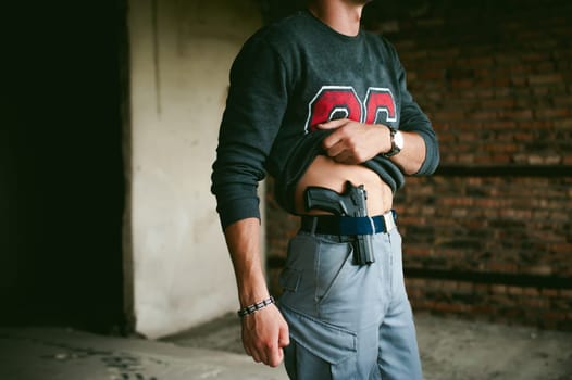 young athletic man holding a gun behind his belt.