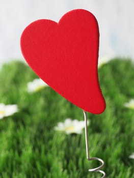 Big red wooden heart shape on a green grass background, Love or Valentines Day concept background