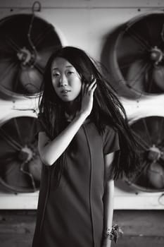 Young beautiful asian woman, on the background of industrial air conditioning system fans. Portrait of a girl with flying hair