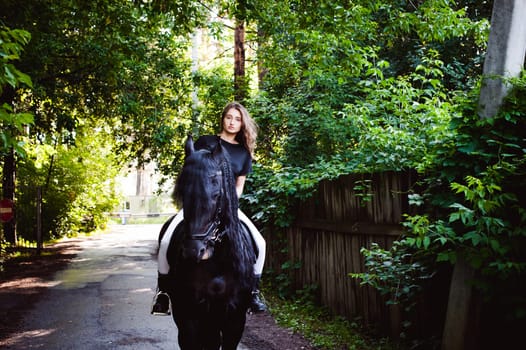 Emotional portrait of a horsewoman rider woman, astride, in love with horses, black Friesian stallion thoroughbred pet, outdoors