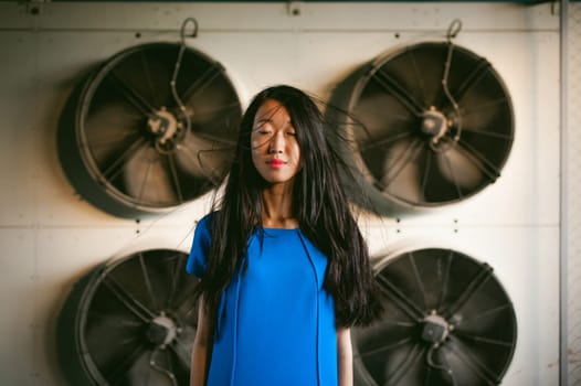 Young beautiful asian woman, on the background of industrial air conditioning system fans. Portrait of a girl with flying hair
