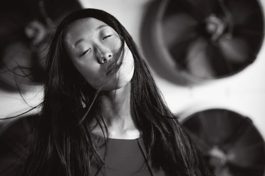 Young beautiful asian woman, on the background of industrial air conditioning system fans. Portrait of a girl with flying hair