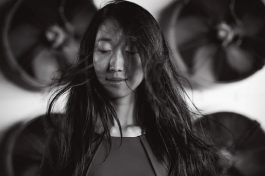 Young beautiful asian woman, on the background of industrial air conditioning system fans. Portrait of a girl with flying hair