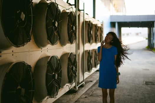 Young beautiful asian woman, on the background of industrial air conditioning system fans. Portrait of a girl with flying hair