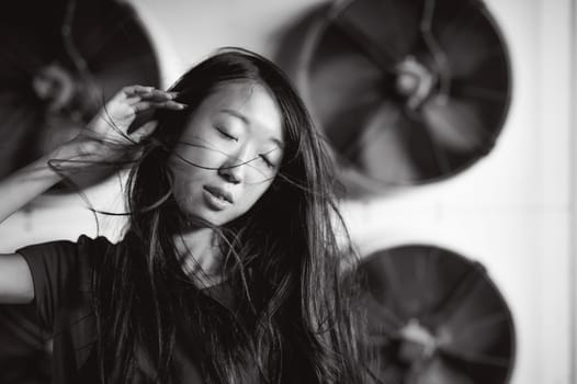 Young beautiful asian woman, on the background of industrial air conditioning system fans. Portrait of a girl with flying hair