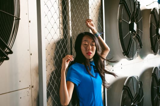 Young beautiful asian woman, on the background of industrial air conditioning system fans. Portrait of a girl with flying hair