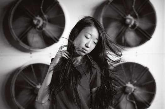 Young beautiful asian woman, on the background of industrial air conditioning system fans. Portrait of a girl with flying hair