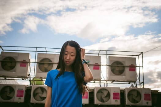 Young beautiful asian woman, on a background of industrial air conditioning system fans