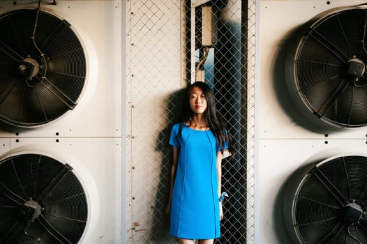 Young beautiful asian woman, on a background of industrial air conditioning system fans