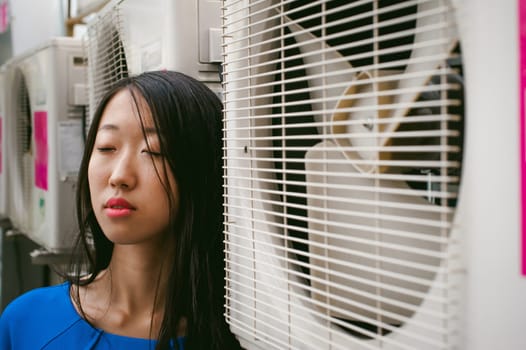 Young beautiful asian woman, on a background of industrial air conditioning system fans