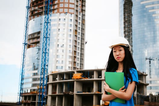 Asian woman in a blue dress and white protective helmet. engineer supervises inspection and control of works at construction site.