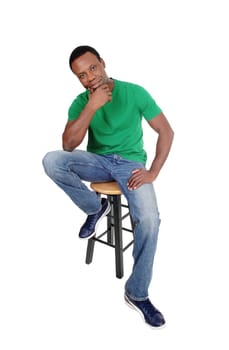 A full body image on a African American man in jeans and green shirt.sitting on chair with his hand on the chin, isolated for white background.