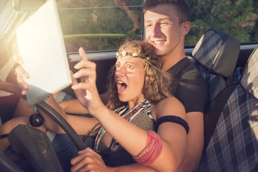 Beautiful young couple looking at a tablet in a car by sunset.