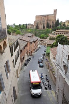 Urban street of old Siena, Tuscany, Italy with urban bus and Basilica of San Domenico in the background. The historic centre of Siena has been declared by UNESCO World Heritage Site