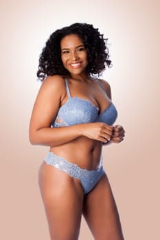 Beautiful happy plus size sexy woman with curly hair in light blue lingerie bra and thong underwear.