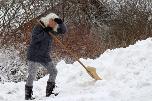 Clearing snow is very exhausting for a woman. A woman is strained by shoveling snow