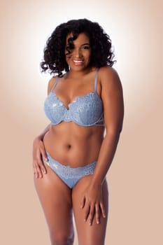 Beautiful happy plus size sexy woman with curly hair in light blue lingerie bra and thong underwear.