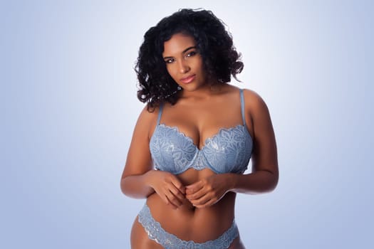 Beautiful happy plus size sexy woman with curly hair in light blue lingerie bra and thong underwear.