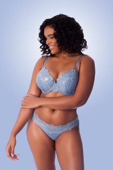 Beautiful happy plus size sexy woman with curly hair in light blue lingerie bra and thong underwear.